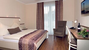 A hotel room with a bed, a desk with a chair, a television, and a window with curtains.
