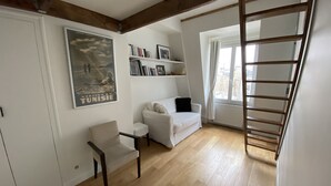 Une pièce avec un canapé blanc, un fauteuil, une bibliothèque, une affiche et un plancher en bois.