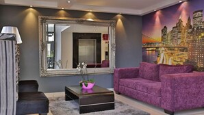A modern living room with a large mirror, a purple sofa, a black coffee table, and a cityscape mural on the wall. - Westay Westpoint Apartments (Johannesburg)