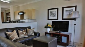 A modern living room with a leather sofa, a flat-screen TV, a coffee table, and a dining area with wooden cabinets and a kitchen in the background. - Westay Westpoint Apartments (Johannesburg)