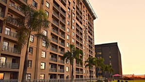 A multi-story hotel with balconies, a well-maintained lawn, and a large building in the background. - Westay Westpoint Apartments (Johannesburg)