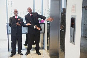 Two men in suits standing in an elevator with a digital display showing the number 11. - Westay Westpoint Apartments (Johannesburg)