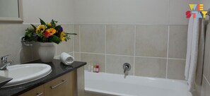 A bathroom with a sink, a bathtub, and a flower vase on the counter. - Westay Westpoint Apartments (Johannesburg)
