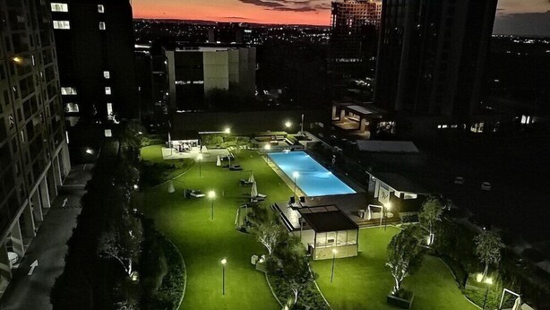 A nighttime view of a residential area with a swimming pool, well-lit pathways, and surrounding greenery. - Westay Westpoint Apartments (Johannesburg)