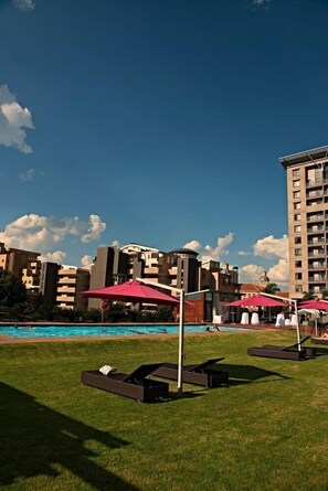 A poolside area with sun loungers and umbrellas, surrounded by modern buildings and a clear sky. - Westay Westpoint Apartments (Johannesburg)
