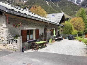 Un bâtiment en pierre avec un toit en pente, une allée en gravier et un banc en bois à l’extérieur.