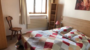 Ein Schlafzimmer mit einem Bett, einem Sessel, einem Fenster und einem Nachttisch mit einer Lampe.