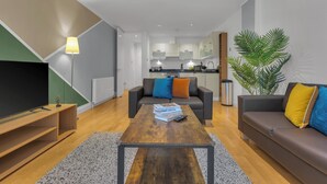 Una sala de estar moderna con un televisor de pantalla plana, una mesa de centro con libros, un sofá y una planta en maceta.