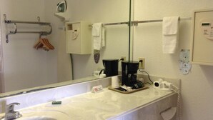 A bathroom with a large mirror, a sink, a towel rack, a coffee maker, and a telephone. - Scottish Inn & Suites IAH West (Houston)