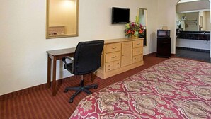 A hotel room with a bed, a desk, a chair, a TV, a dresser, and a mirror. - Scottish Inn & Suites IAH West (Houston)