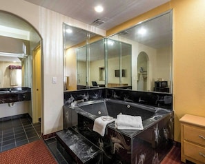 A bathroom with a large bathtub, a mirror, and a sink. - Scottish Inn & Suites IAH West (Houston)