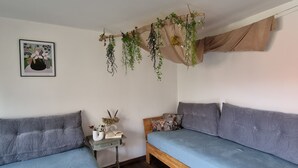 A room with two grey sofas, a small wooden table with a vase and book, and a hanging plant arrangement. - 2 Zimmer FeWo mit Außenpool und Sauna (Sulzfeld am Main)