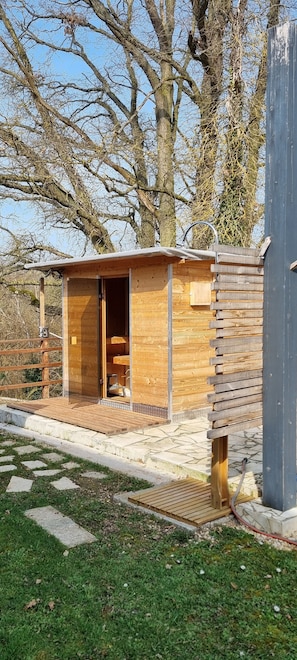 Una pequeña cabaña de madera con la puerta abierta, un banco afuera y un sendero de piedra que la conduce.