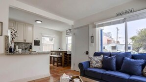 Un salon moderne avec un canapé bleu, une table basse et un coin cuisine visible à travers une porte ouverte.