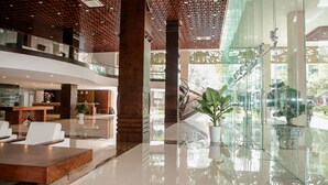 A modern hotel lobby with a reception desk, seating area, and a glass staircase leading to an upper level. - Elephants Hotel Buon Ma Thuot (Buon Ma Thuot)