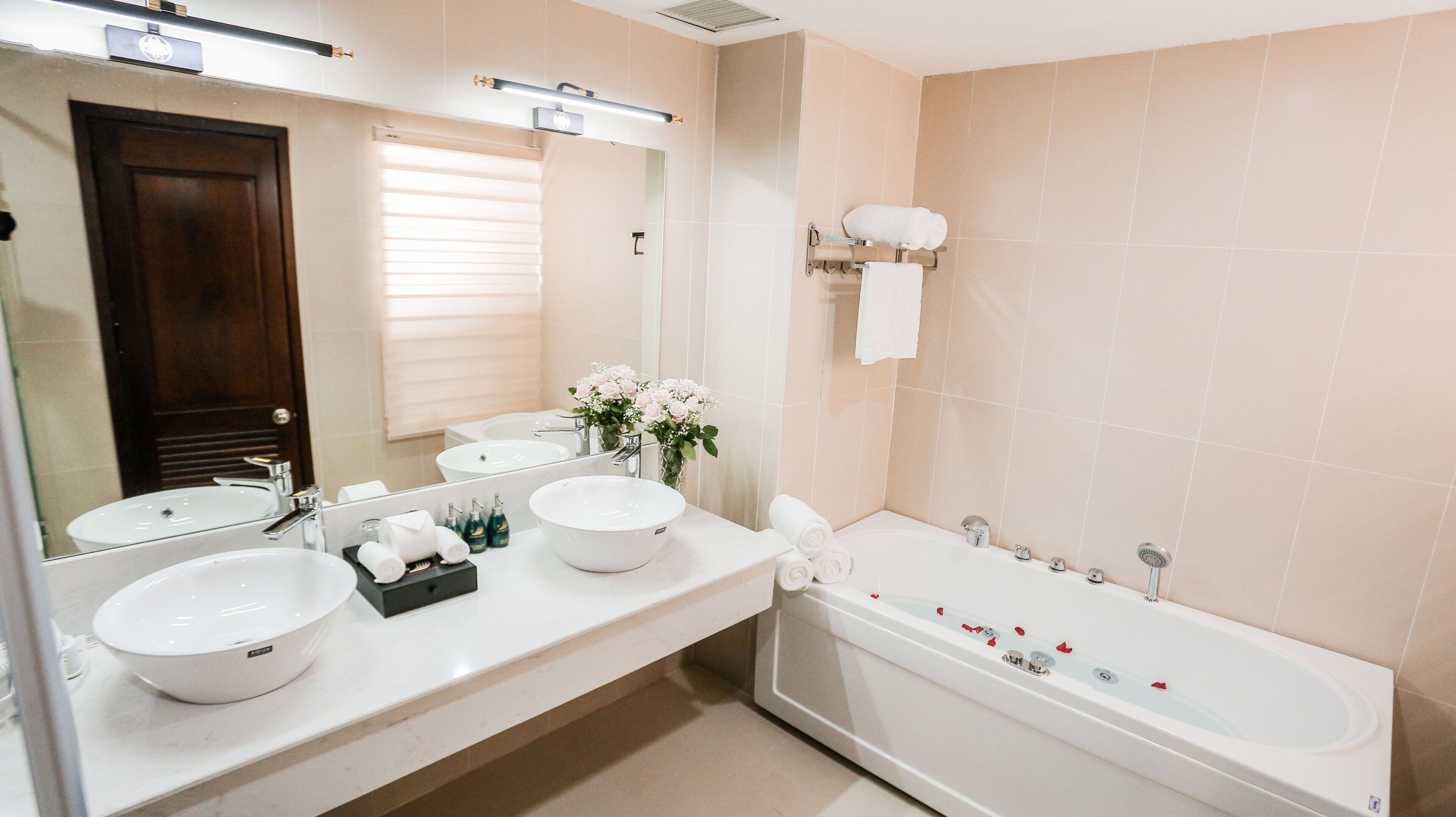 A modern bathroom with two sinks, a large mirror, a bathtub, and a window with blinds.