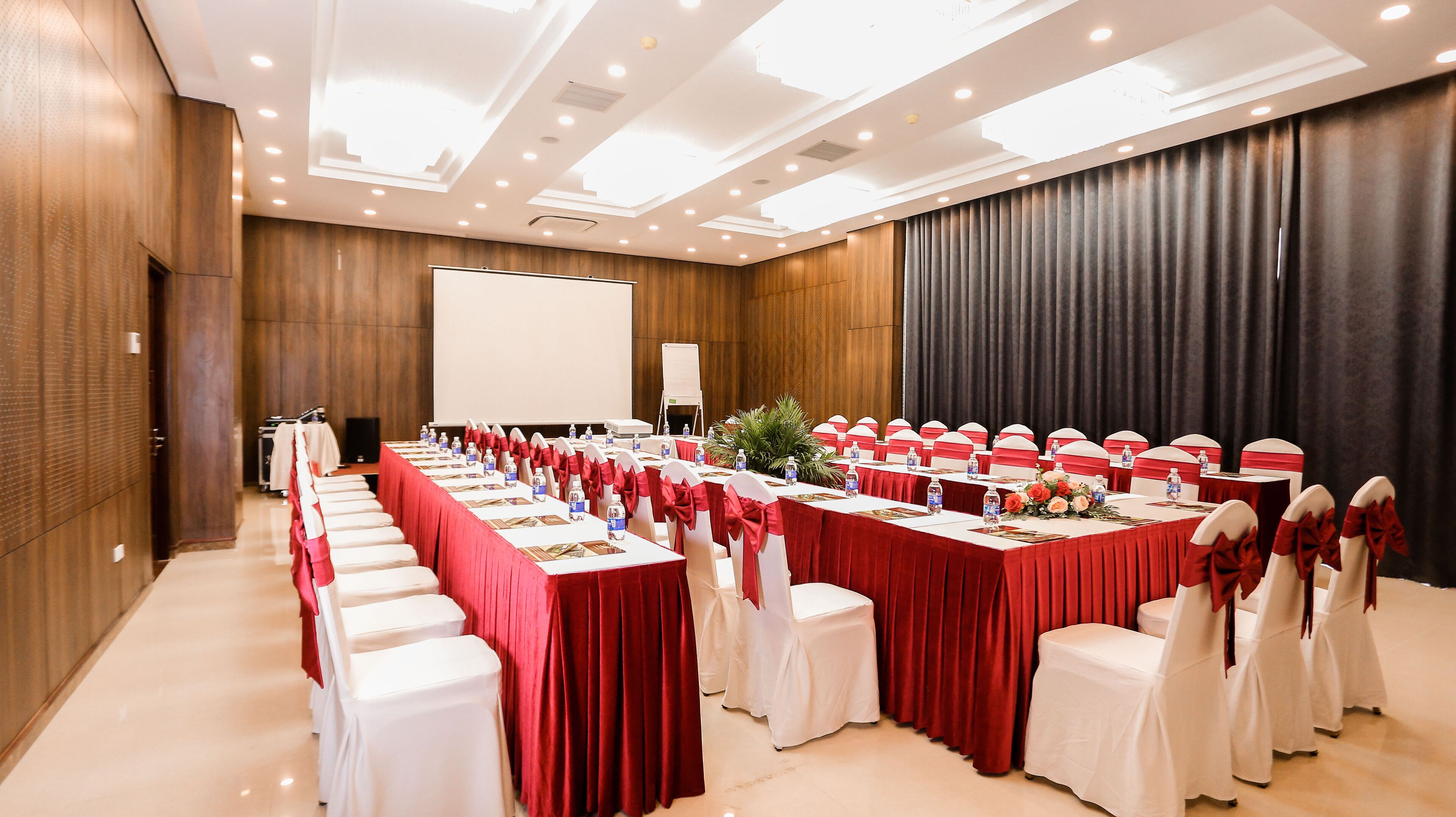 A conference room with long tables, white chairs, and red tablecloths.