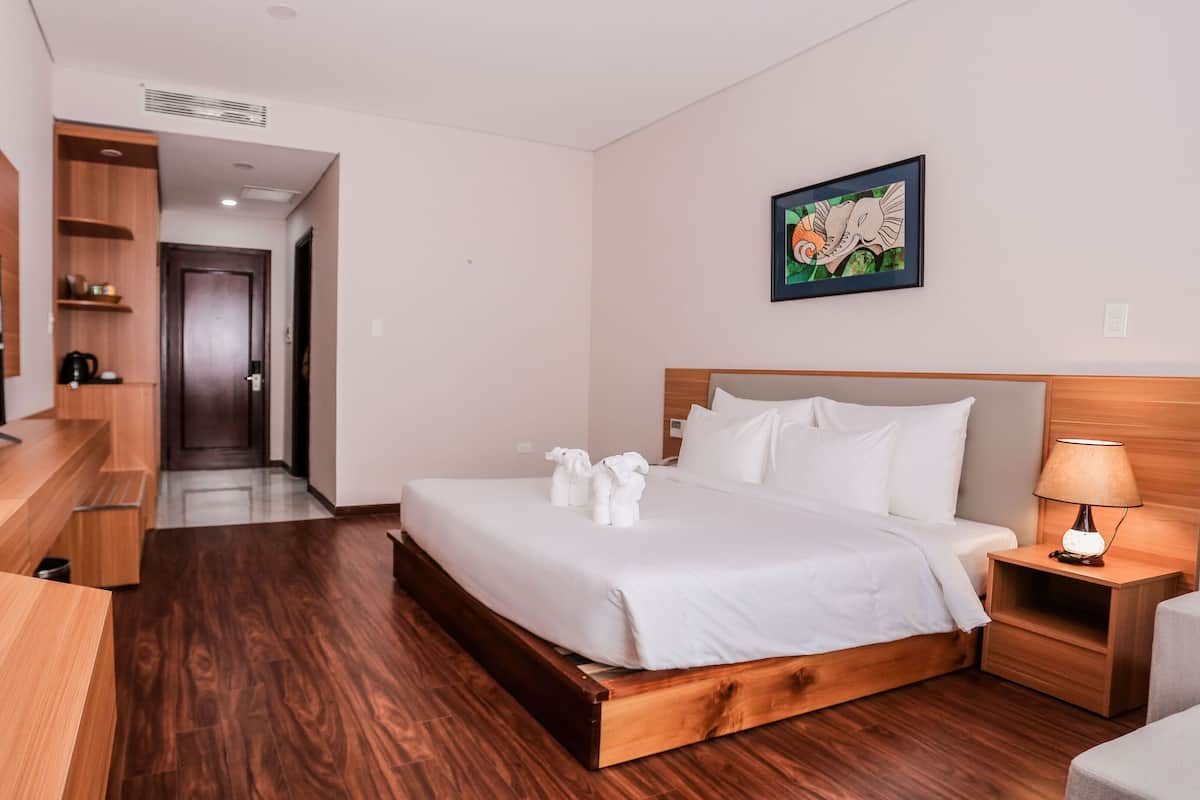 A hotel room with a wooden bed, a television, a desk, and a painting on the wall.
