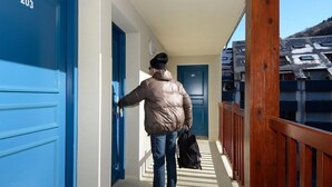 Une personne marche dans un couloir où les portes sont bleues, l’une étant marquée du numéro 203 et l’autre du numéro 201.