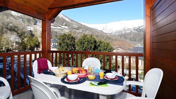 Une terrasse en bois avec une table dressée pour le petit-déjeuner, offrant une vue sur un paysage montagneux enneigé.