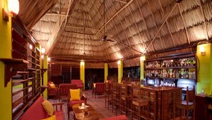 Un restaurant doté d’un toit de chaume, de meubles en bois et d’un espace bar.