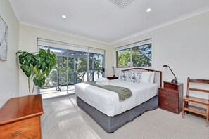A bedroom with a large bed, a nightstand, a wooden chair, and a potted plant.
