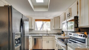 A modern kitchen with stainless steel appliances, white cabinetry, and a large window providing natural light. - Tucson Foothills Oasis Near Hiking Trails! (Tucson)