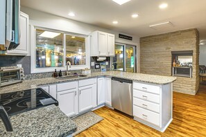 A modern kitchen with white cabinetry, a built-in dishwasher, and a stone accent wall. - Featured on TV! Epic Indoor Pool • Sleeps 24 (Bridgman)