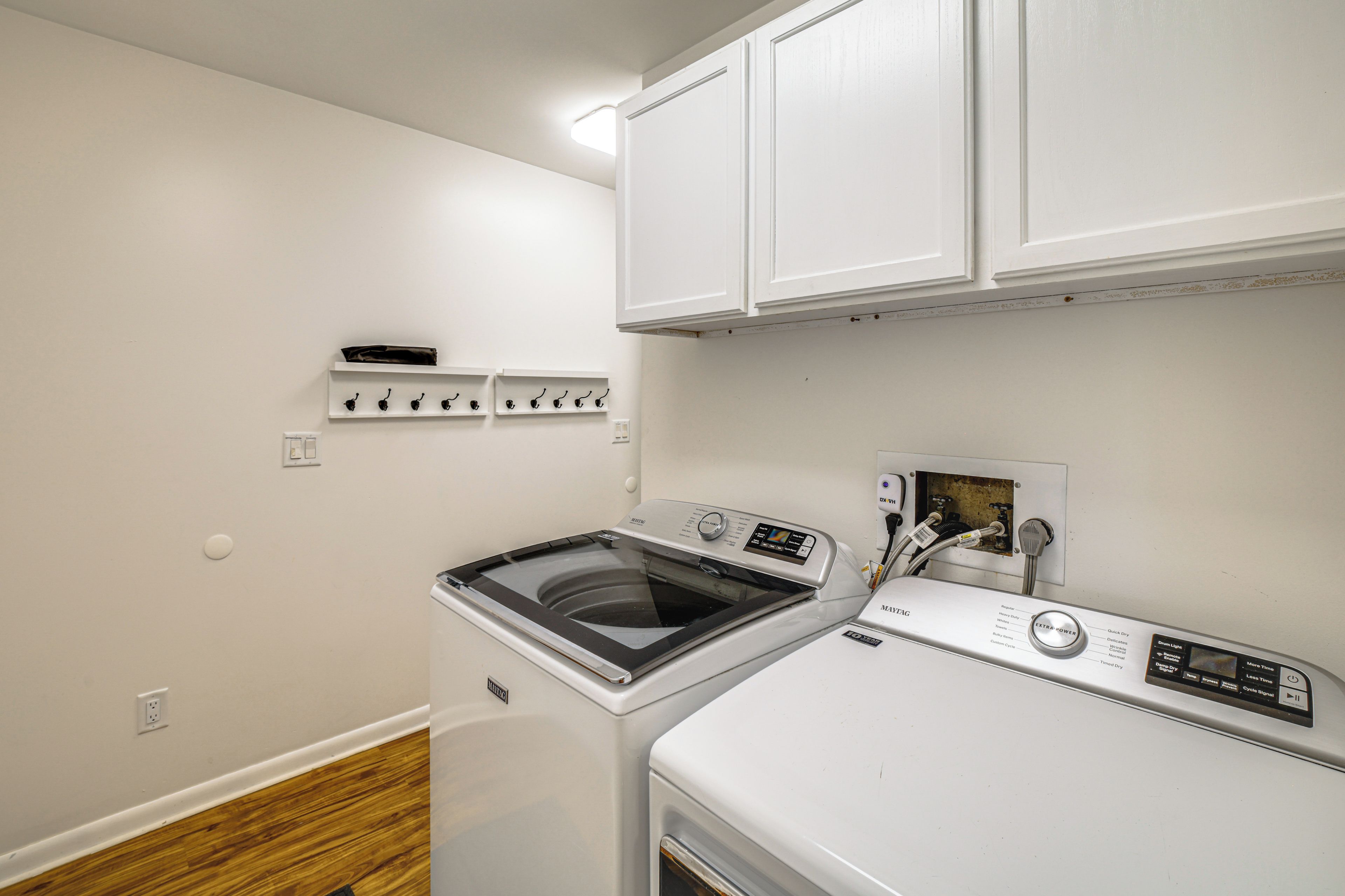 A compact laundry room with a front-loading washer and dryer, a white wall with a shelf above the dryer, and a wooden floor.