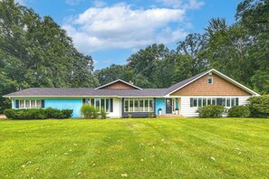 Une maison à deux étages dotée d’un porche abrité, d’une pelouse bien entretenue et d’un paysage boisé en arrière-plan.