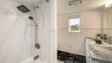 Ein Badezimmer mit Dusche, Waschbecken und Fenster.