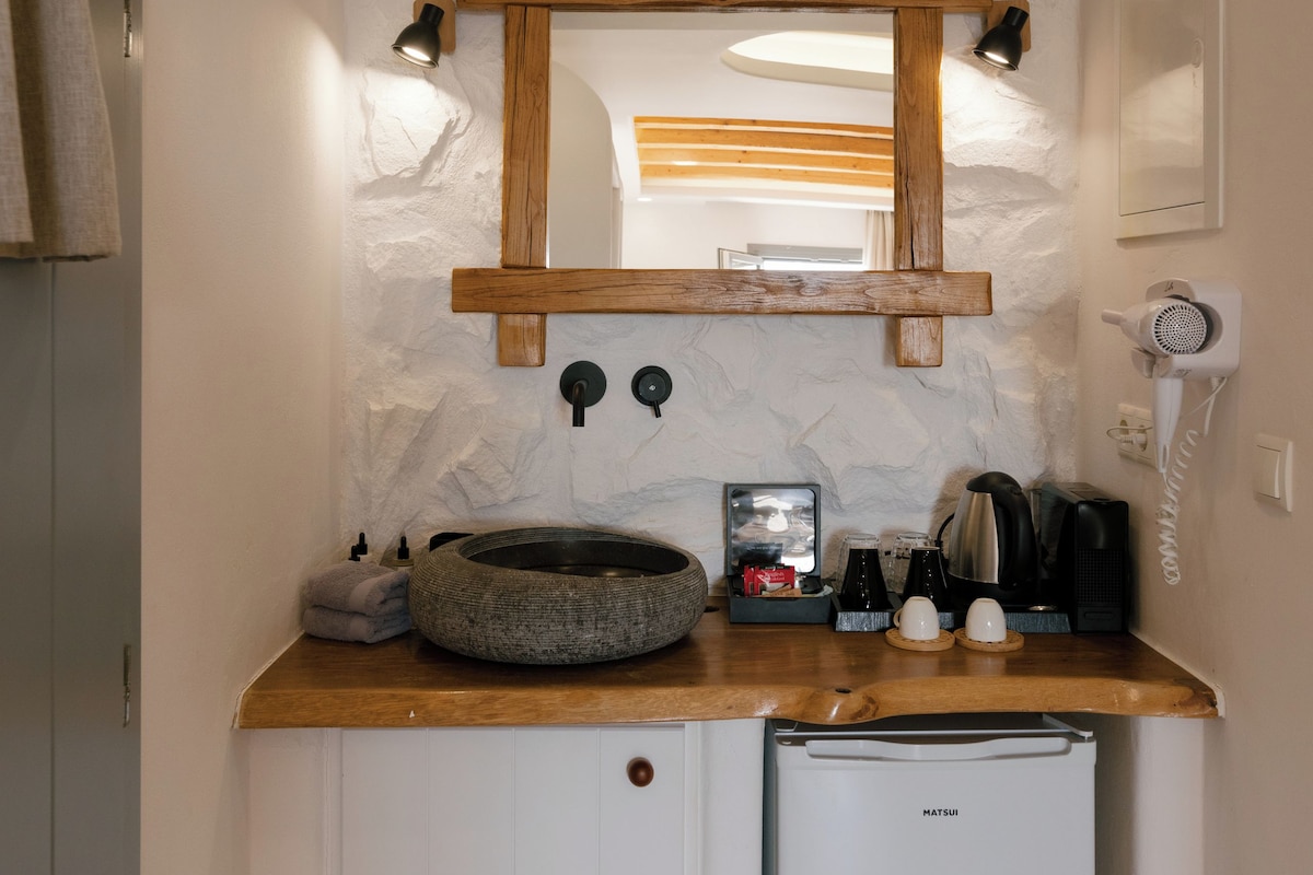 Un baño pequeño con un lavamanos de piedra, un espejo, un secador de pelo y un refrigerador compacto.
