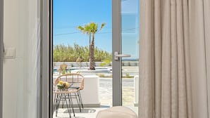 A bedroom with a sliding glass door leading to a balcony with outdoor furniture and a palm tree.