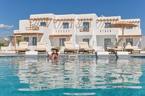 A poolside area with lounge chairs and a building with white walls and wooden balconies. - Naxos Finest Hotel & Villas (Naxos)