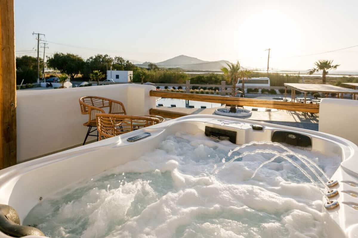 Un jacuzzi con una pérgola de madera sobre él, rodeado de mobiliario exterior y vistas al paisaje.