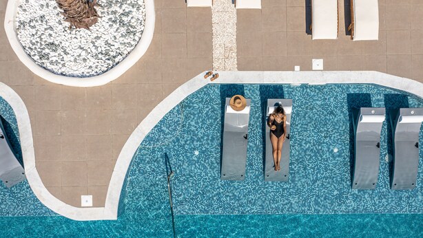 An aerial view of a swimming pool with a tiled deck, lounge chairs, and a circular seating area.
