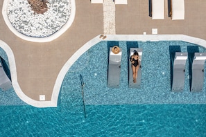 Vista aérea de una piscina con solárium, sillones de descanso y un área de estar circular.