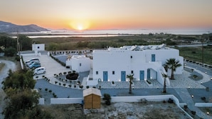 A white building with blue doors, a parking area, and a view of the sunset over the sea.