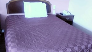 Una cama bien hecha con cabecera, una mesita de noche con lámpara, y un aplique de pared.