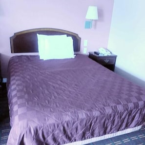 A neatly made bed with a headboard, a bedside table with a lamp, and a wall-mounted light fixture. - Americas Best Value Inn Seaside North (Seaside)