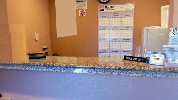 A hotel reception area with a calendar, a 'Pacific Lodging Supply' sign, a 'Please Ring Bell' sign, and a 'Cafe' sign. - Americas Best Value Inn Seaside North (Seaside)