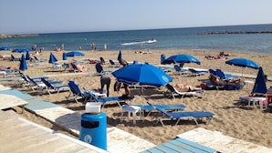 Een strand met blauwe parasols en ligbedden.