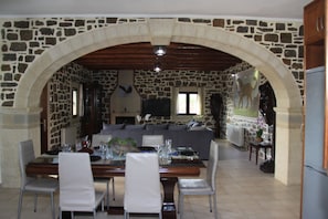 A dining area with a stone archway, a wooden ceiling, a stone wall, a sofa, and a television.