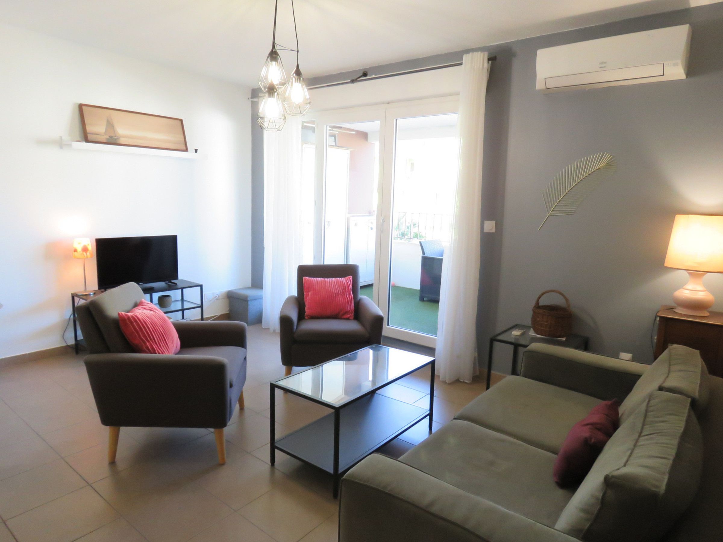 A modern living room with a flat-screen TV, two armchairs, a sofa, a glass coffee table, and a lamp.