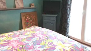 Une chambre avec des murs de couleur turquoise, une couvre-lit à motifs floraux, un téléviseur et une fenêtre avec des rideaux.