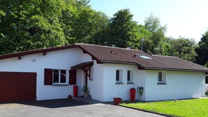 Une maison de plain-pied avec un toit recouvert de tuiles rouges, une porte de garage et un petit porche agrémenté de plantes en pot.