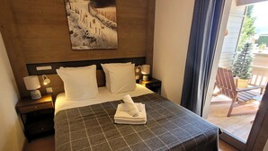A hotel room with a bed, two bedside tables with lamps, a painting on the wall, and a view of the outside. - Beautiful bright apartment in the center, with parking (Les Gets)