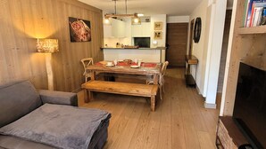A cozy living room with a sofa, a wooden dining table, and a kitchen in the background. - Beautiful bright apartment in the center, with parking (Les Gets)