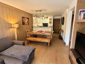 A cozy living room with a sofa, a wooden dining table, and a kitchen in the background. - Beautiful bright apartment in the center, with parking (Les Gets)