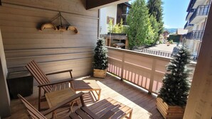 A wooden deck with outdoor seating, two potted Christmas trees, and a view of a building with balconies. - Beautiful bright apartment in the center, with parking (Les Gets)